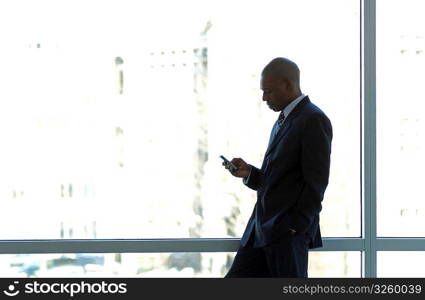 Businessman silhouetted in large office window, using PDA smart phone.