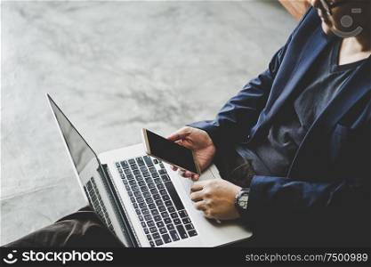 Businessman sit on cement floor with smartphone and using laptop , selective focusing .