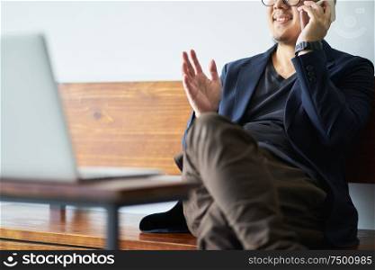 Businessman sit on wooden chair using smartphone in front of the laptop.