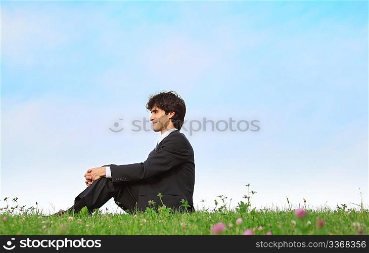 businessman sits on grass, view in profile