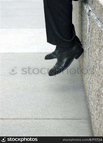Businessman sits on the ledge with his feet inches from the ground