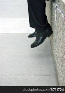 Businessman sits on the ledge with his feet inches from the ground