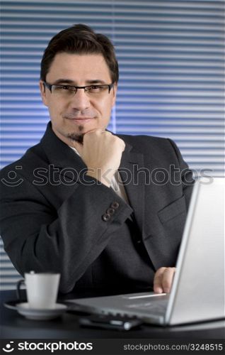 Businessman sitting at desk in office and drinking coffee.