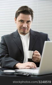 Businessman sitting at desk in office and drinking coffee.