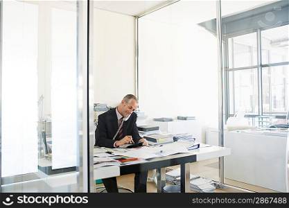 Businessman sitting at desk in office talking on phone.