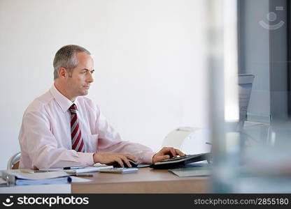 Businessman sitting at desk in office using computer.