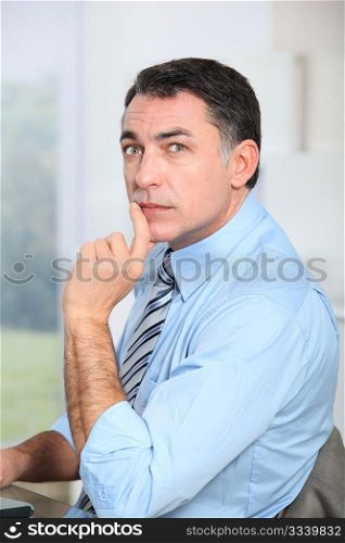 Businessman sitting at his desk with hand on chin