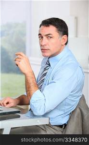 Businessman sitting at his desk with hand on chin