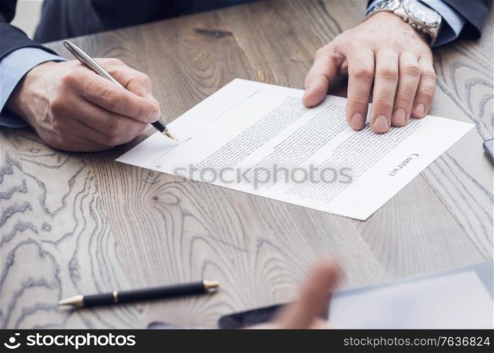 Businessman sitting at office desk signing a contract with shallow focus on pen. Businessman signing a contract