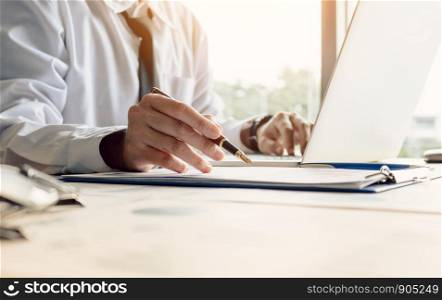 Businessman sitting at office room holding pen pointing summary report graph and analyze with using laptop for searching information data.