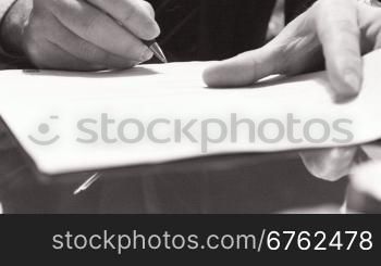 Businessman sitting at shiny office desk signing a contract with noble pen