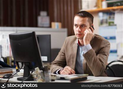 Businessman sitting behind his desk in the office talking on a mobile phone listening to the conversation with a serious expression