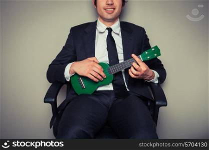 Businessman sitting in an office chair is playing ukulele