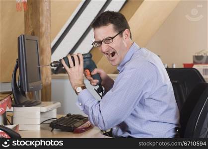Businessman sitting in front of a computer and holding a drill