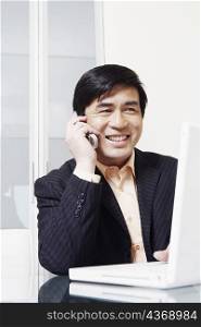 Businessman sitting in front of a laptop talking on a mobile phone