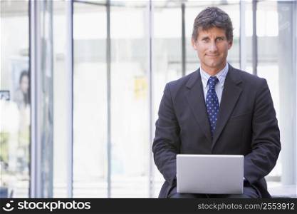 Businessman sitting in office lobby using laptop smiling
