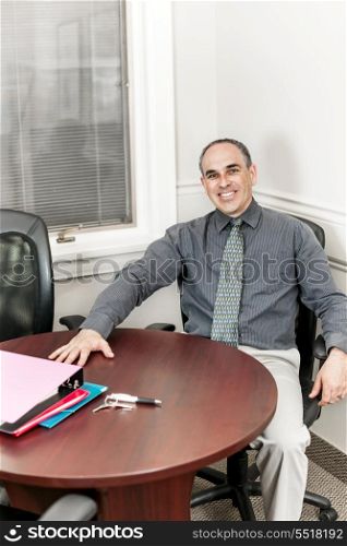 Businessman sitting in office meeting room. Smiling middle aged business man sitting at table in office meeting room