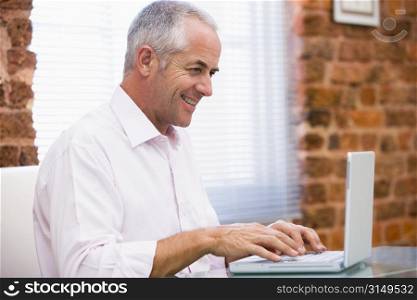 Businessman sitting in office typing on laptop smiling