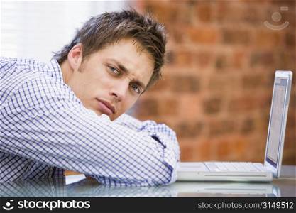 Businessman sitting in office with laptop looking unhappy
