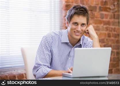 Businessman sitting in office with laptop smiling