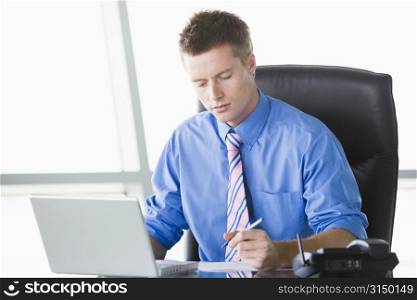 Businessman sitting in office with laptop writing note