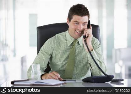 Businessman sitting in office with personal organizer on telephone