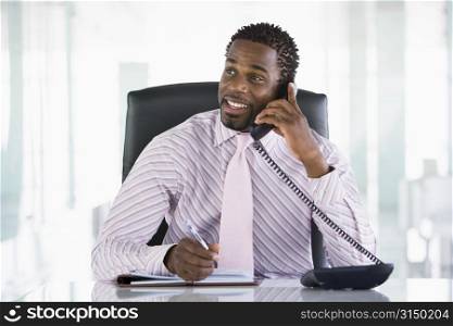 Businessman sitting in office with personal organizer open on telephone