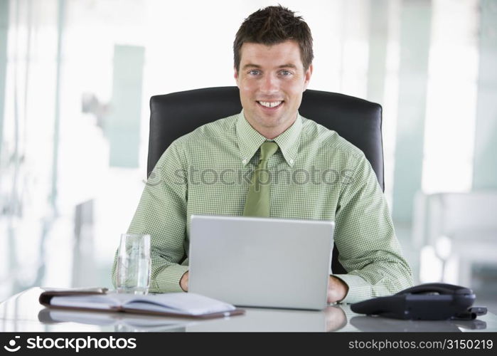 Businessman sitting in office with personal organizer using laptop smiling