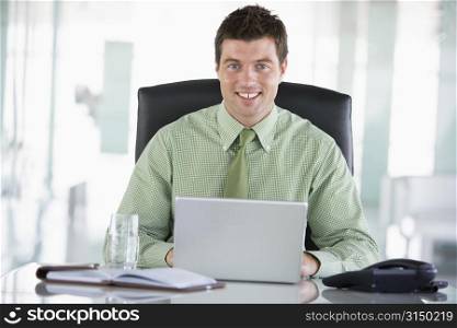 Businessman sitting in office with personal organizer using laptop smiling