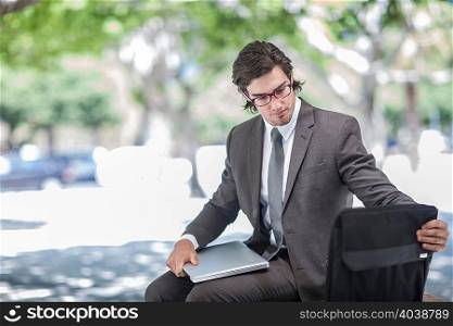 Businessman sitting in park removing laptop from briefcase