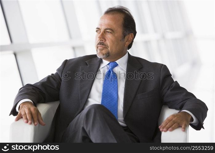 Businessman sitting indoors looking out window (high key/selective focus)