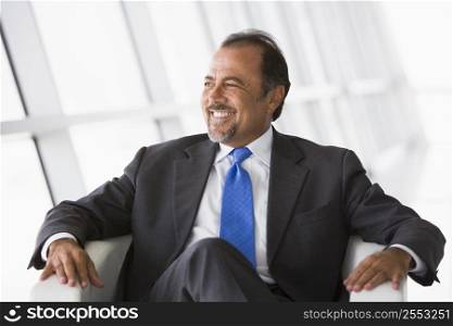 Businessman sitting indoors looking out window smiling (high key/selective focus)