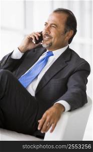 Businessman sitting indoors on cellular phone smiling (high key/selective focus)