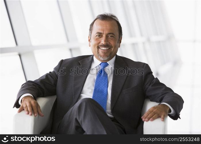 Businessman sitting indoors smiling (high key/selective focus)