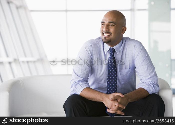 Businessman sitting indoors smiling (high key/selective focus)