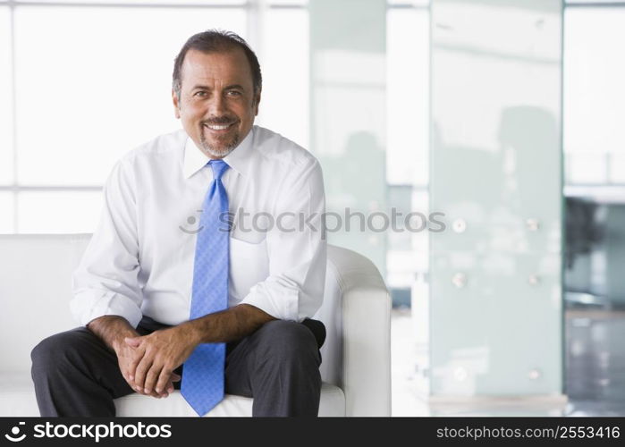 Businessman sitting indoors smiling (high key/selective focus)