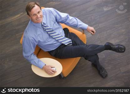 Businessman sitting indoors with cellular phone smiling