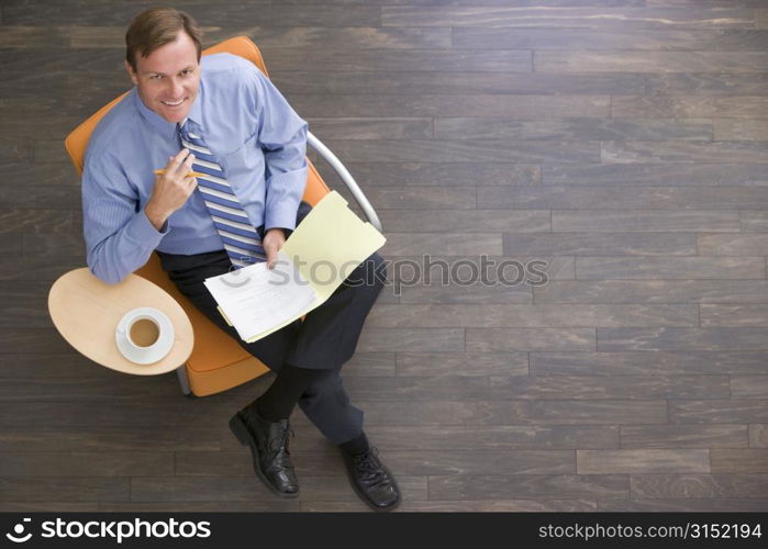 Businessman sitting indoors with coffee and folder smiling