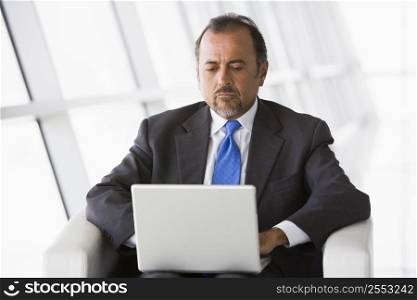 Businessman sitting indoors with laptop (high key/selective focus)