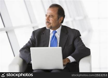 Businessman sitting indoors with laptop looking out window (high key/selective focus)