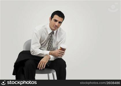 Businessman sitting on a chair and holding a disposable cup