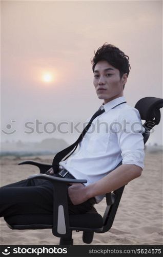 Businessman sitting on a chair and looking at camera in the middle of the desert