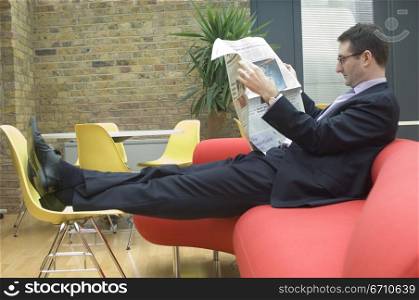 Businessman sitting on a couch and reading a newspaper