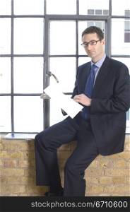 Businessman sitting on a window sill and holding a document