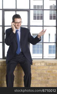 Businessman sitting on a window sill and talking on a mobile phone
