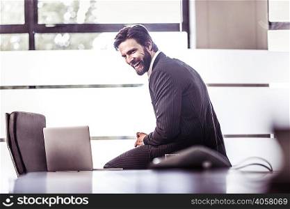 Businessman sitting on boardroom table laughing