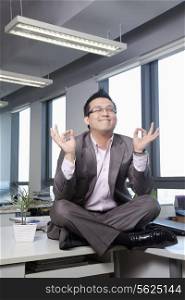Businessman sitting on desk in the office meditating