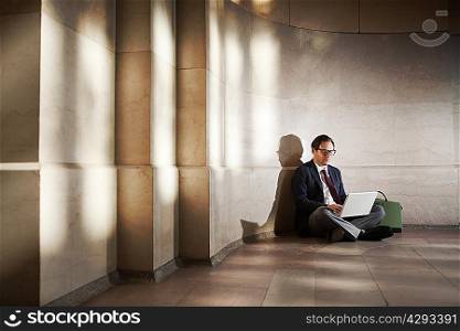 Businessman sitting on floor by wall using laptop
