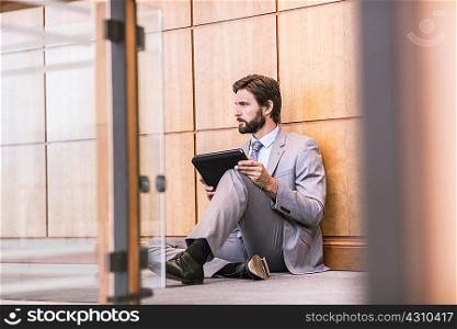 Businessman sitting on office floor using digital tablet