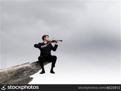 Businessman sitting on rock edge and playing violin